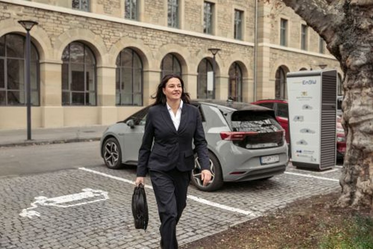 Frau im schwarzen Anzug vor Amtsgebäude, E-Auto und Ladesäule